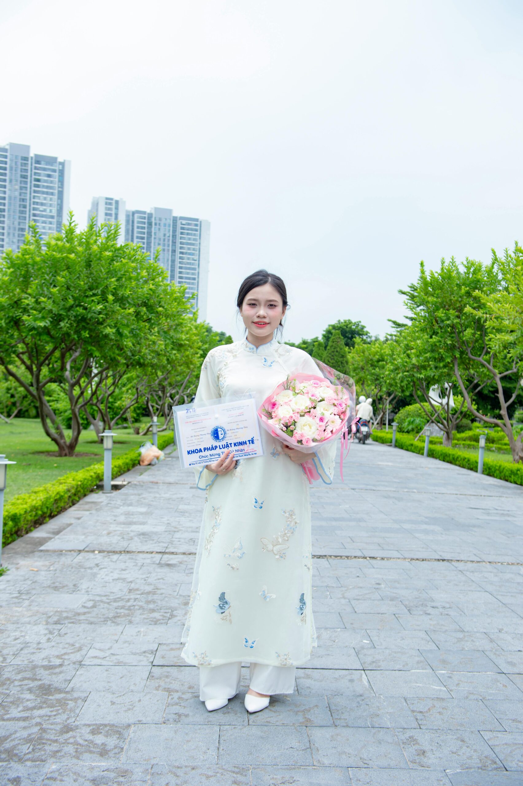 Elegant woman in traditional Ao Dai holding flowers in a scenic park in Hanoi, Vietnam.